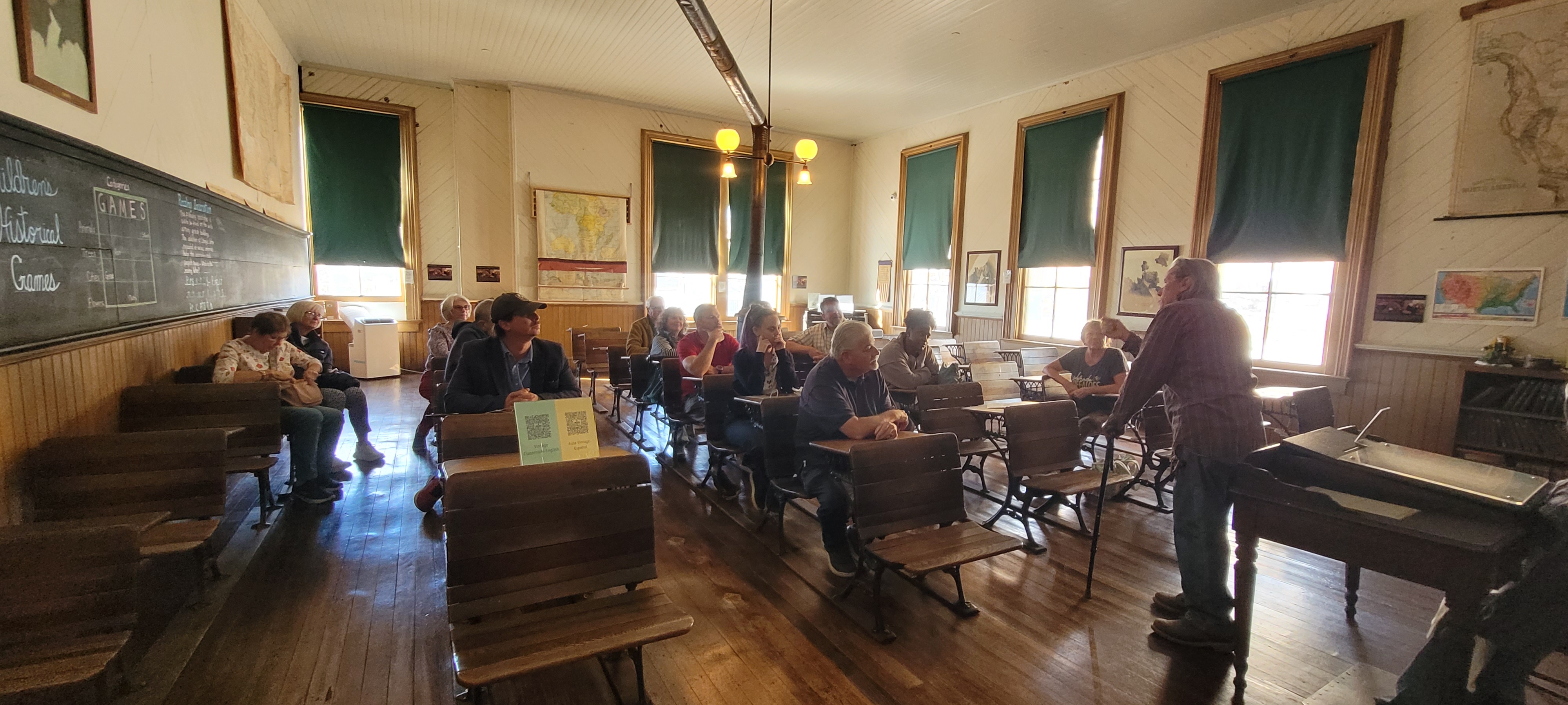 People seated at old wooden school desks in a Victorian classroom.